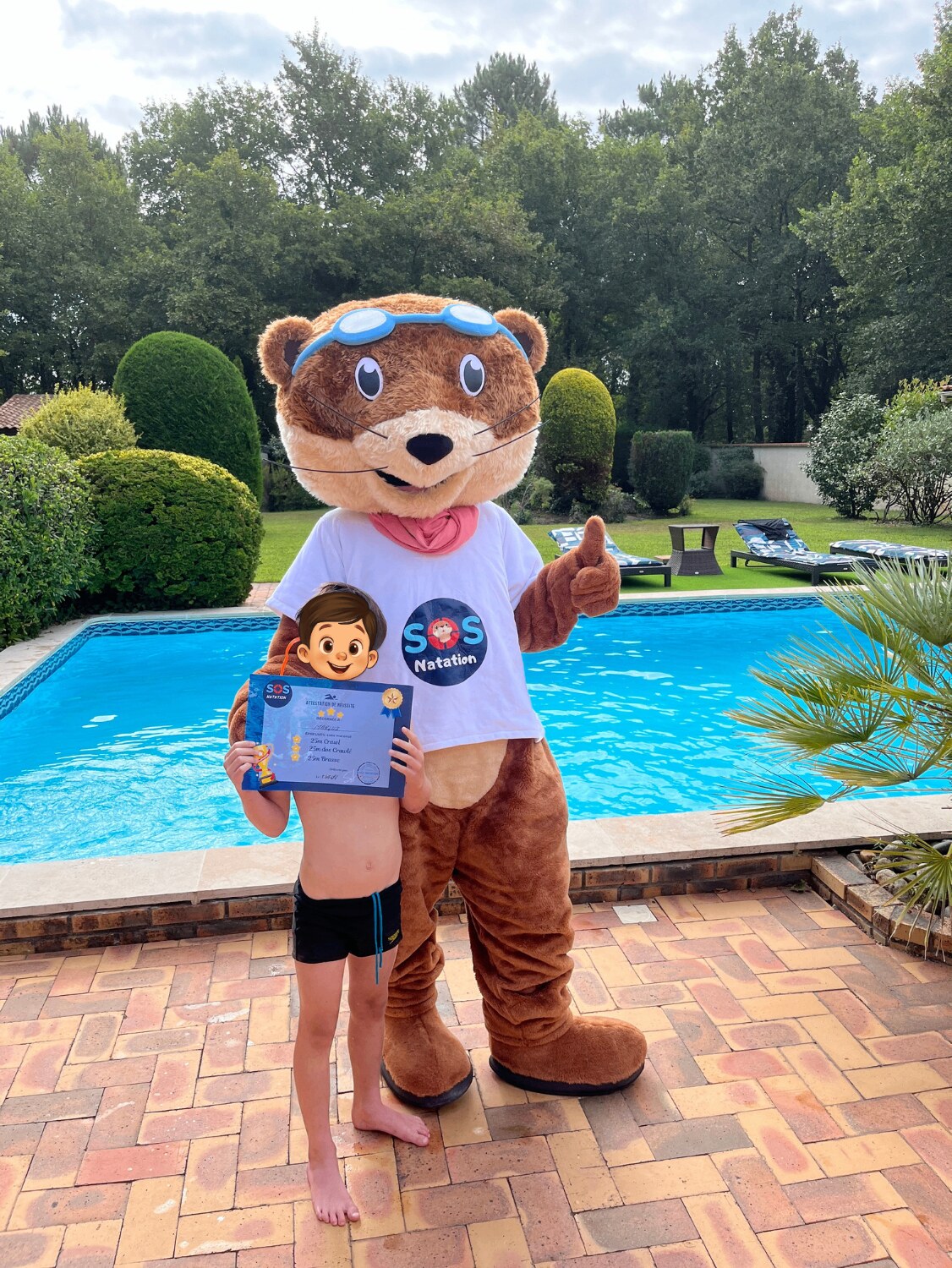 Un enfant fier de son attestation de réussite avec Louloute, la mascotte de SOS Natation, au bord de la piscine sur le Bassin d’Arcachon